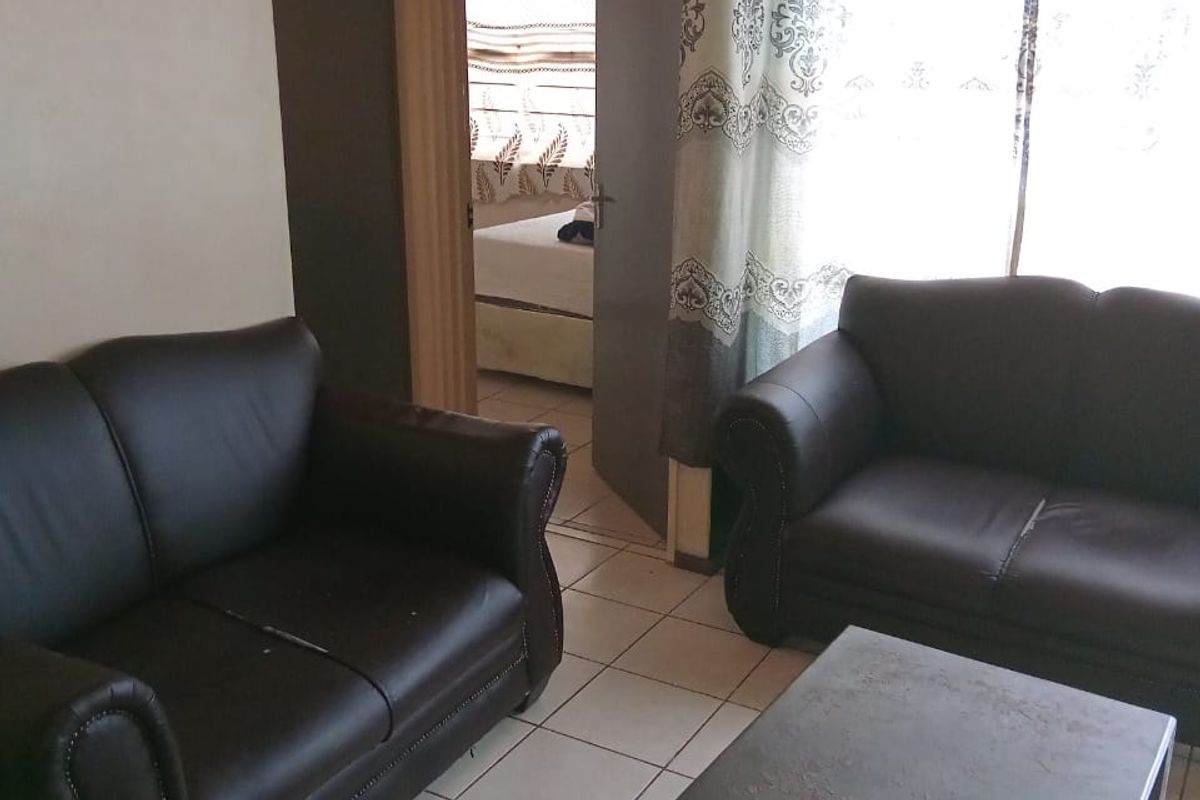 A living room area featuring ceramic floor tiles and access to an adjacent bedroom, showing signs of wear on the walls.