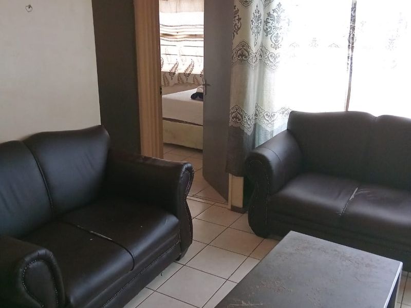 A living room area featuring ceramic floor tiles and access to an adjacent bedroom, showing signs of wear on the walls.