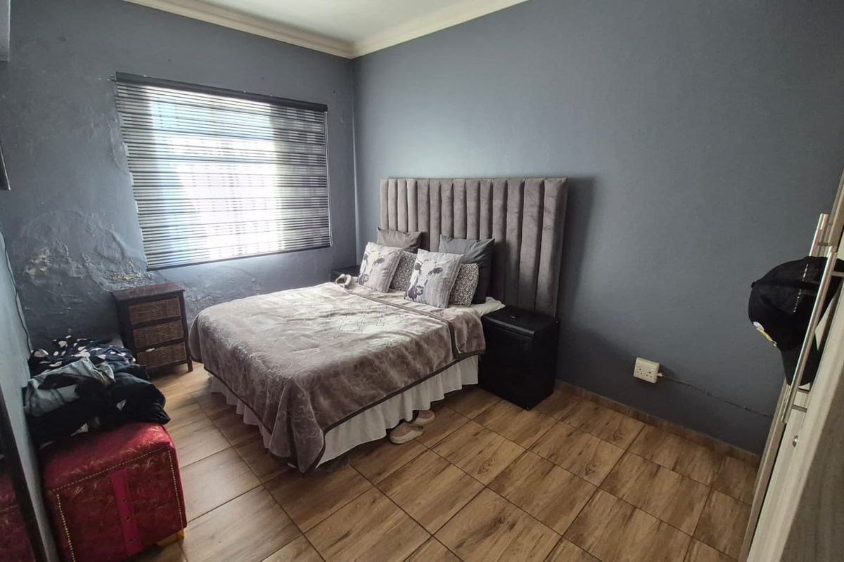 A bedroom featuring wood-look tile flooring and venetian blinds, currently showing visible wall plaster damage and paint deterioration requiring repair.