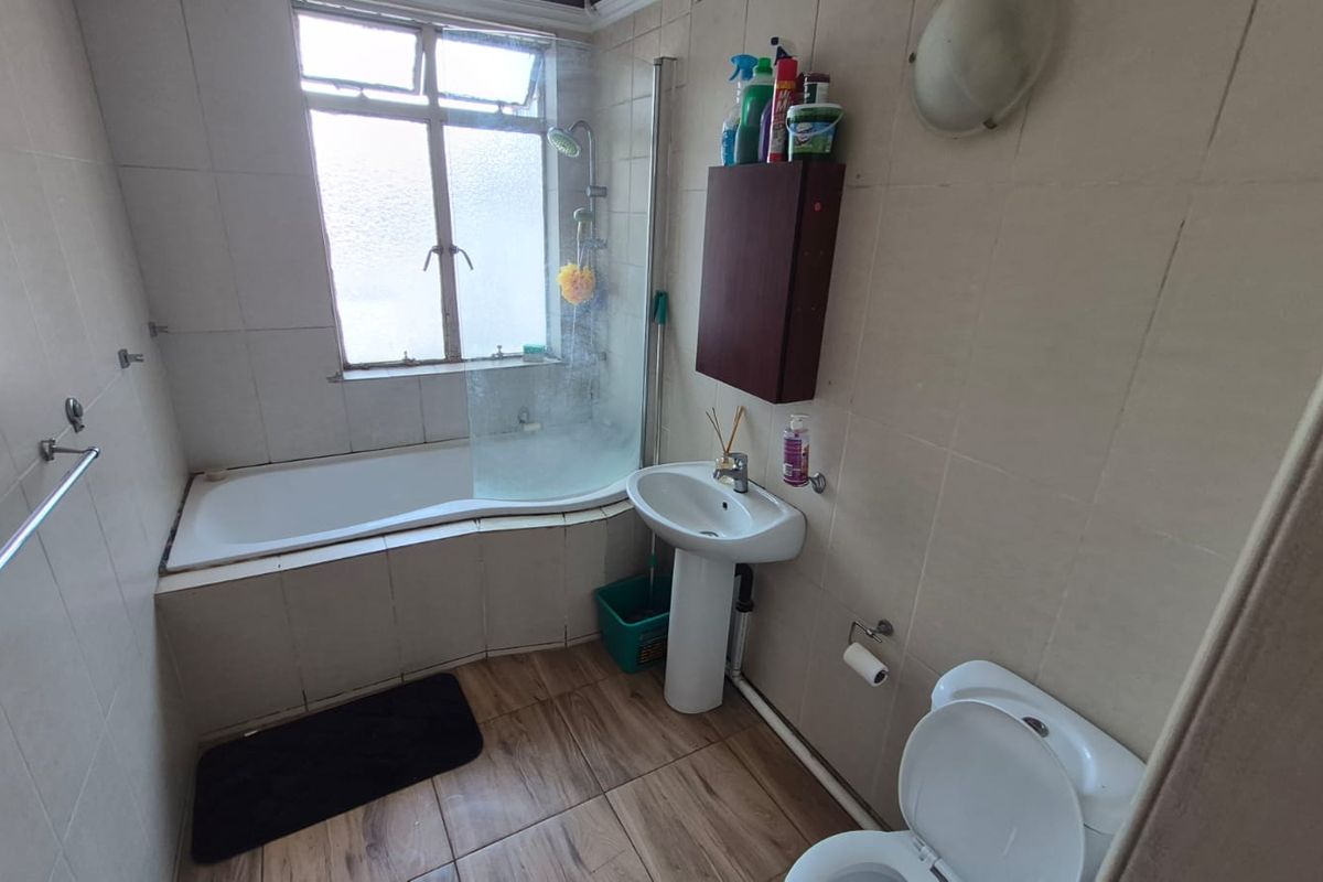 A functional bathroom featuring a bathtub with a shower screen, pedestal basin, toilet, and tiled finishes throughout.