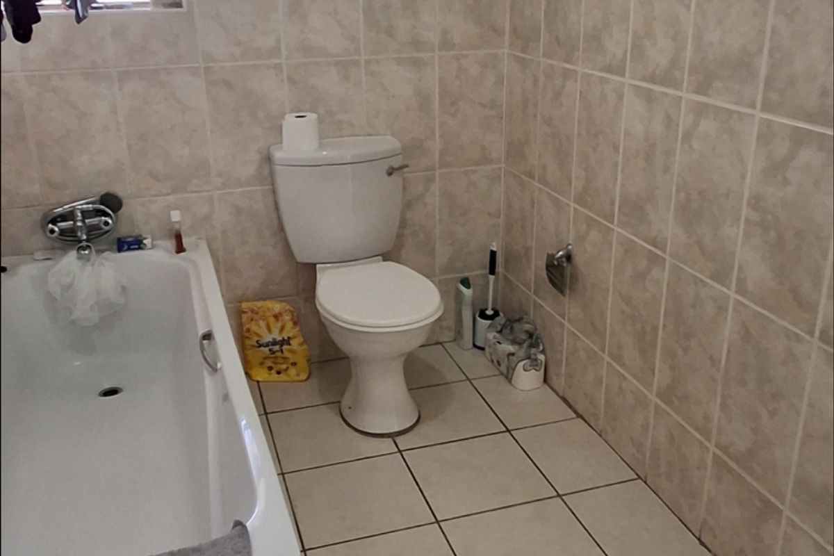A functional bathroom featuring a bathtub, toilet, and neutral ceramic tiling throughout the walls and floor.