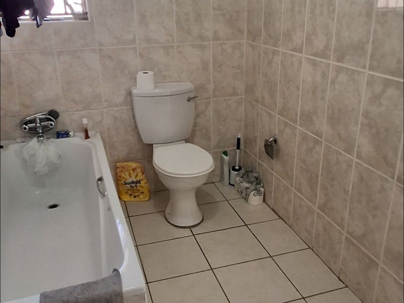 A functional bathroom featuring a bathtub, toilet, and neutral ceramic tiling throughout the walls and floor.