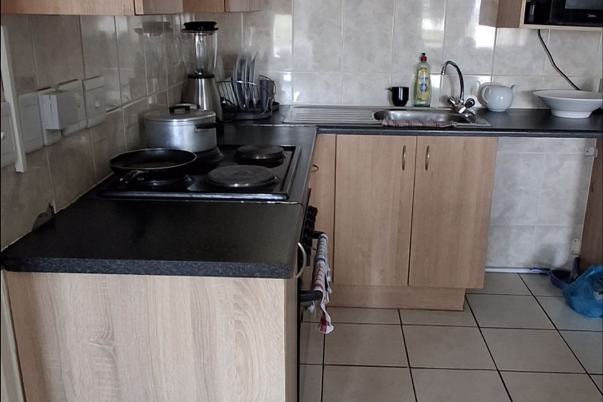 A functional kitchen featuring light wood-look cabinetry, dark laminate countertops, ceramic tile flooring, and a built-in hob and oven.