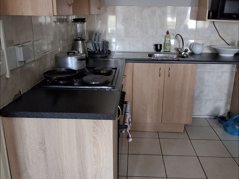A functional kitchen featuring light wood-look cabinetry, dark laminate countertops, ceramic tile flooring, and a built-in hob and oven.