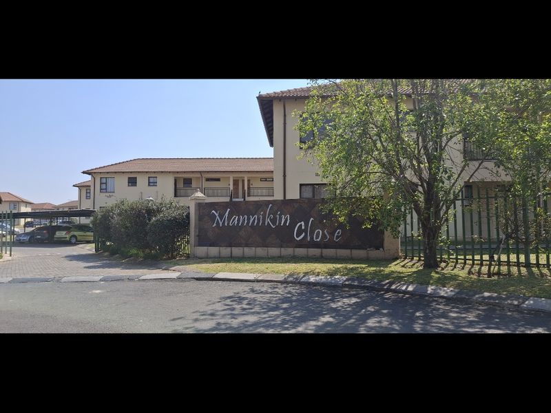 Street view of the Mannikin Close apartment complex entrance, featuring secure perimeter fencing and established landscaping.