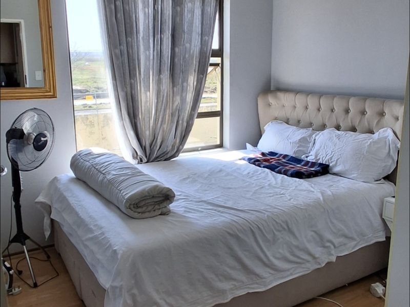 A functional bedroom featuring laminate flooring, a large window with curtain rod, and a central ceiling light fixture.