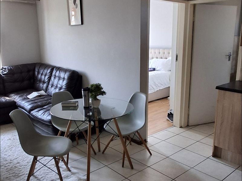 Open plan living and dining area featuring neutral tiled flooring and coved ceilings, with direct access to an adjacent bedroom.