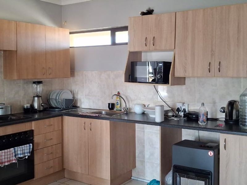A functional kitchen featuring light wood-finish cabinetry, dark laminate countertops, a built-in oven, and tiled backsplash, offering a practical layout for daily use.