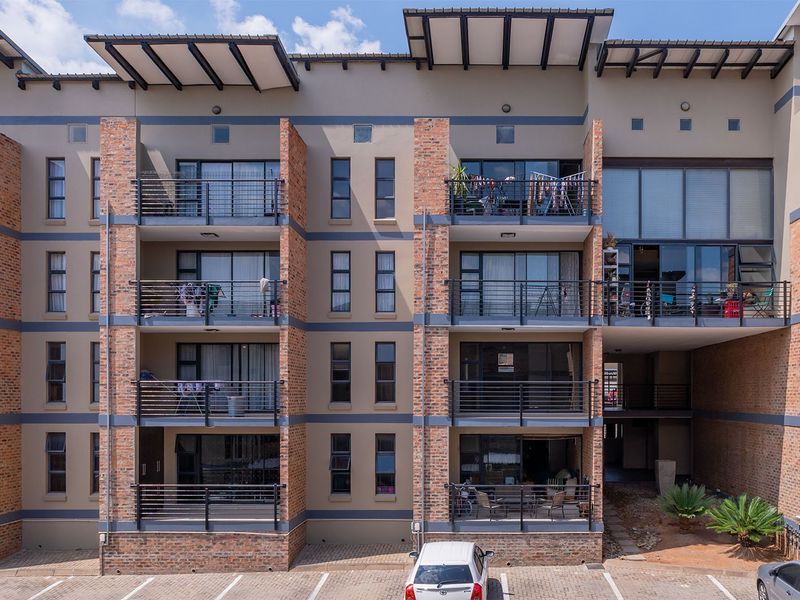 A modern multi-story apartment building facade featuring exposed brickwork, private balconies with metal railings, and large sliding glass doors.