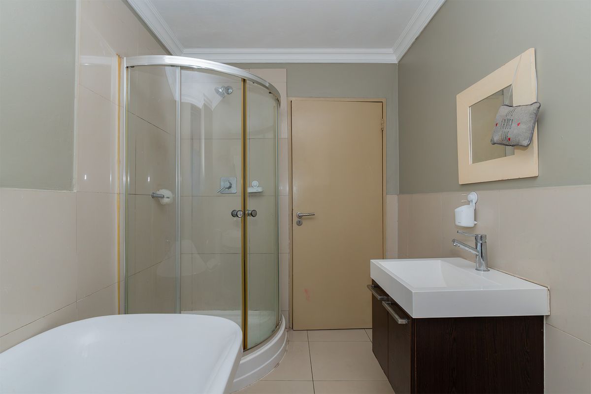 A functional bathroom featuring a curved glass shower enclosure, a modern vanity with basin, and neutral wall tiling.