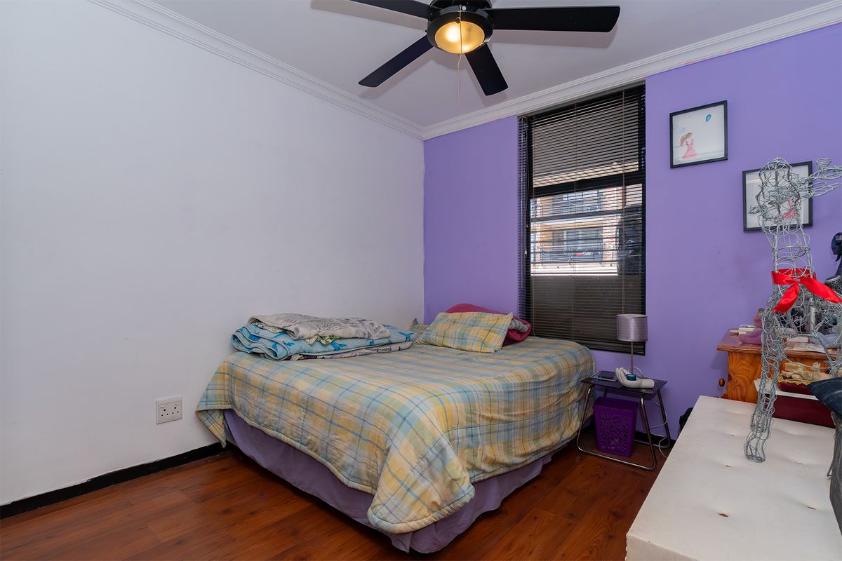 A bedroom featuring laminate flooring, a ceiling fan, and a window with venetian blinds, offering a functional space with potential for modernization.