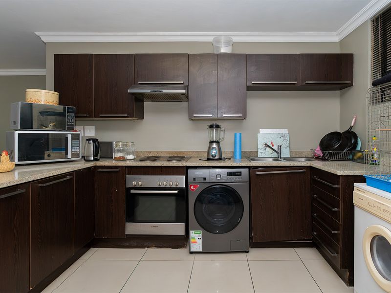 A functional kitchen featuring dark wood cabinetry, stone countertops, integrated oven, and hob, with tiled flooring and neutral wall finishes.