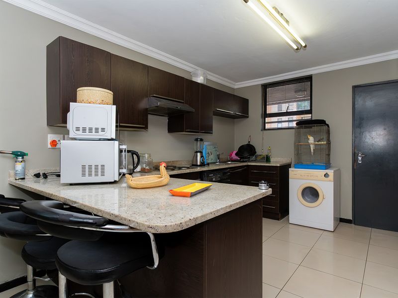 A functional kitchen featuring dark wood cabinetry, granite countertops, and tiled flooring, providing a practical workspace with integrated storage and preparation areas.
