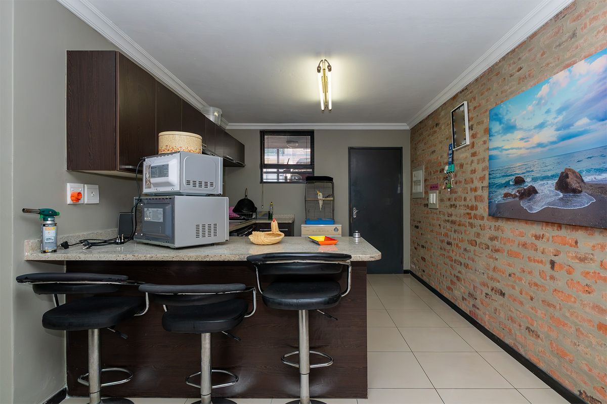 A functional kitchen featuring dark wood cabinetry, granite countertops with a breakfast bar, and a distinctive exposed brick feature wall.