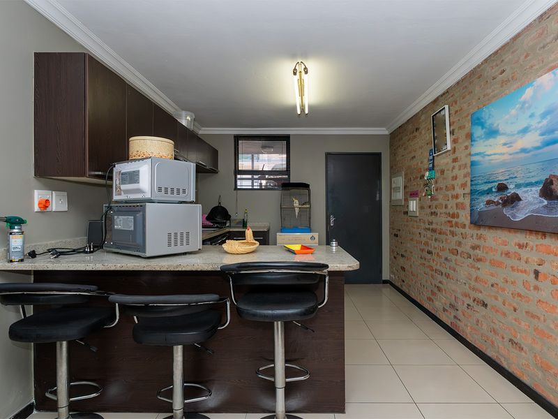 A functional kitchen featuring dark wood cabinetry, granite countertops with a breakfast bar, and a distinctive exposed brick feature wall.