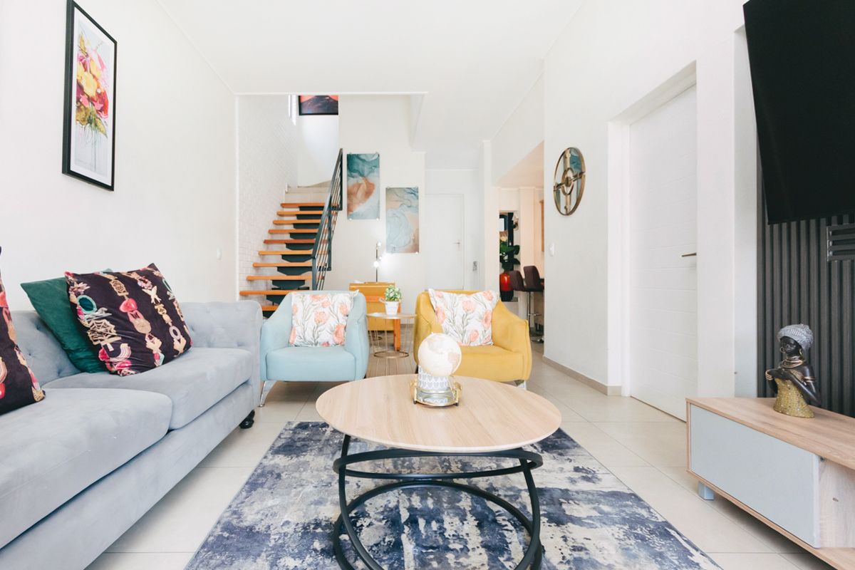 A bright and modern living room featuring tiled flooring, a feature slatted wall, and an open staircase leading to the upper level.