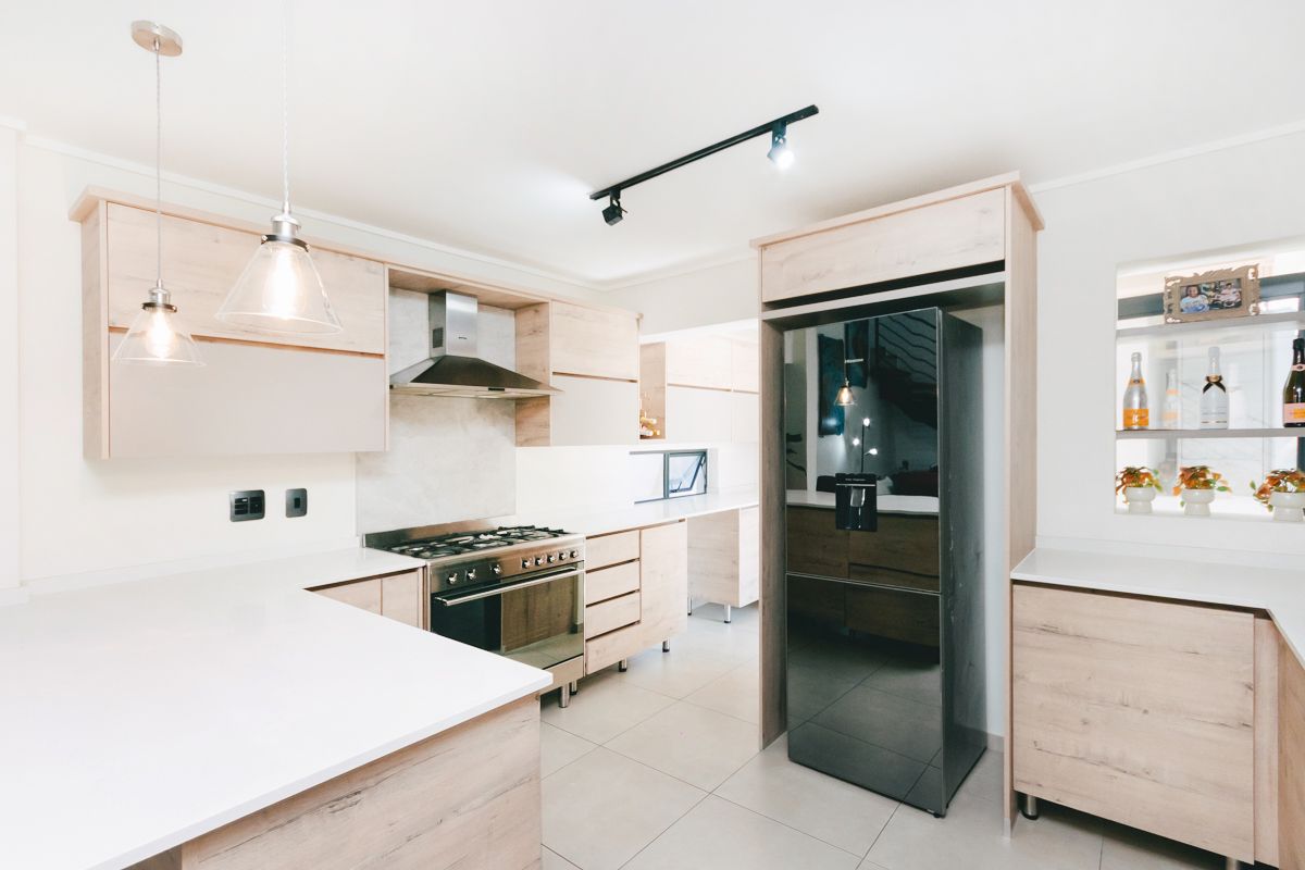 Modern kitchen featuring light wood cabinetry, stone countertops, a gas stove with extractor fan, and contemporary track and pendant lighting.