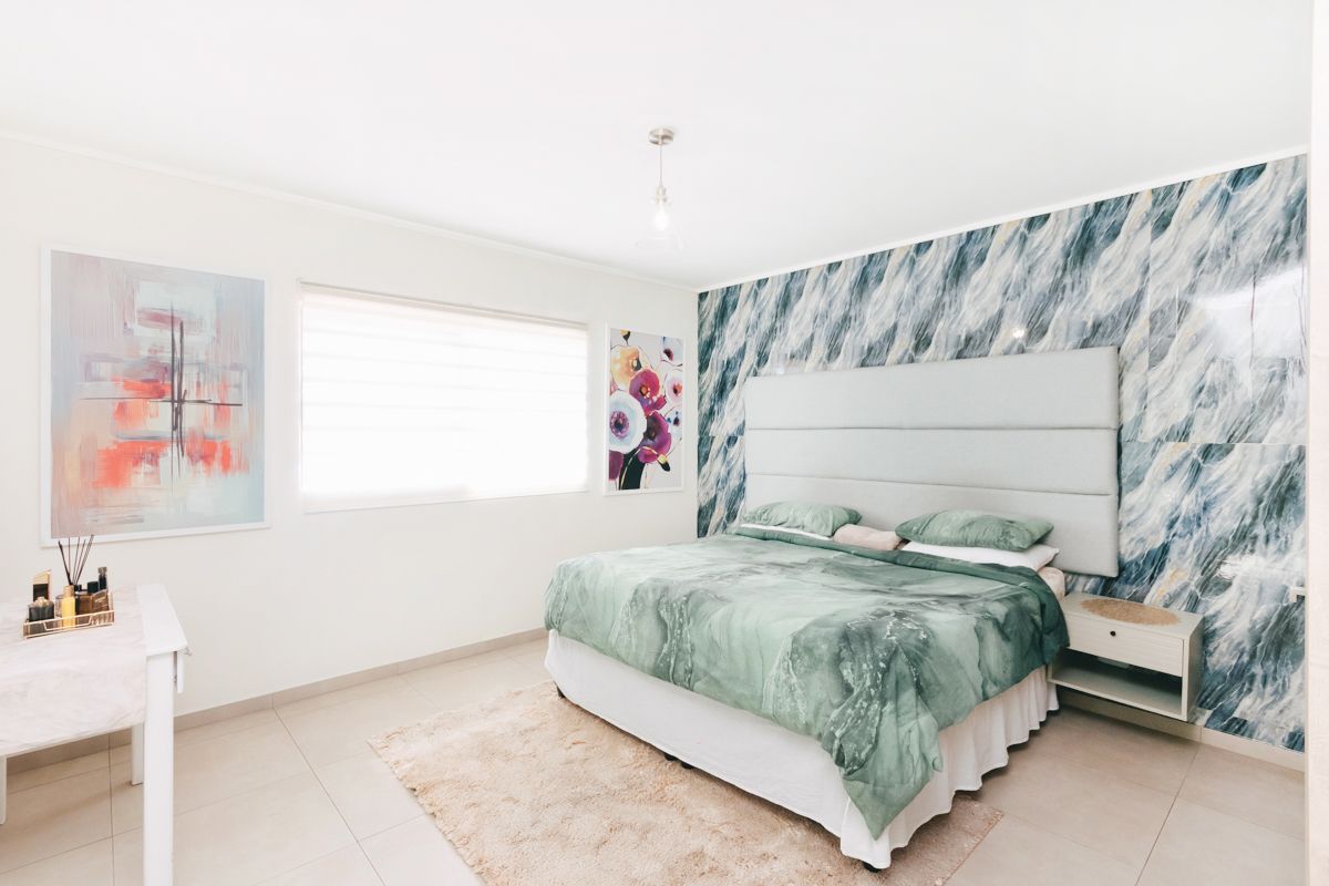 A well-maintained bedroom featuring a striking marble-effect feature wall, neutral tiled flooring, and modern roller blinds.