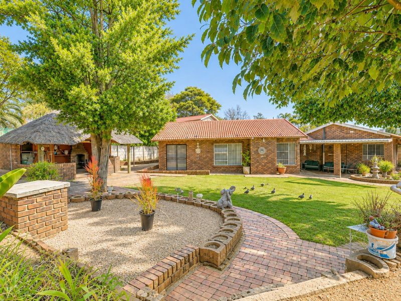 Spacious rear garden featuring a facebrick house, a covered patio, and a traditional thatched lapa with a built-in braai area.