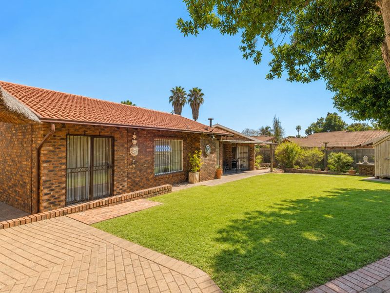 A well-maintained rear exterior view featuring a face brick facade, terracotta roof tiles, a paved patio area, and a spacious lawn with a garden shed.