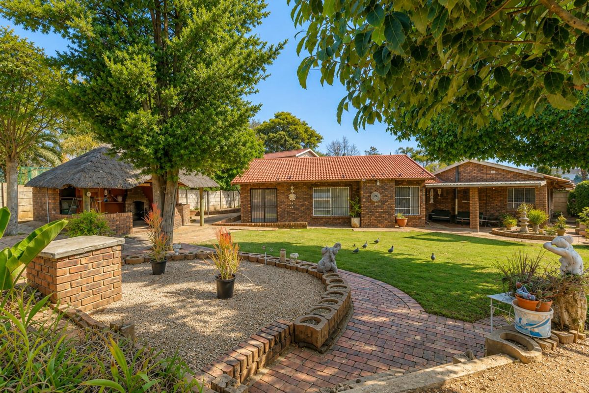 A well-maintained rear garden featuring a brick-faced house, a traditional thatched lapa, and established landscaping with paved pathways.