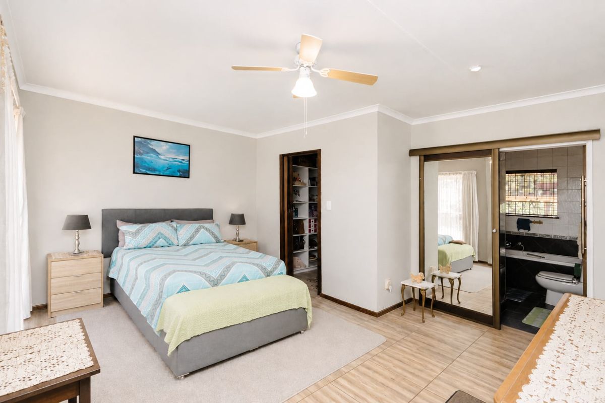 Spacious bedroom featuring a ceiling fan, built-in wardrobe with sliding mirror doors, and an attached en-suite bathroom with tiled flooring.