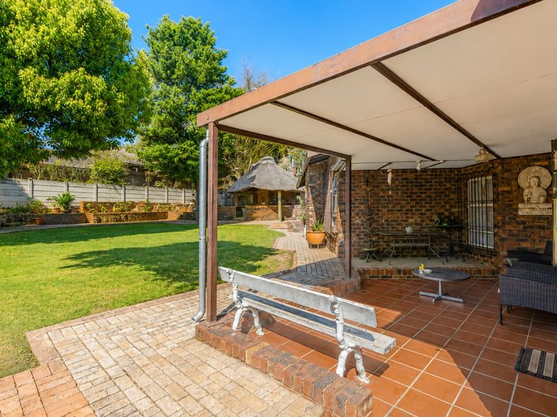 A covered brick patio area featuring tiled flooring, overlooking a well-maintained garden with a lawn and retaining wall.