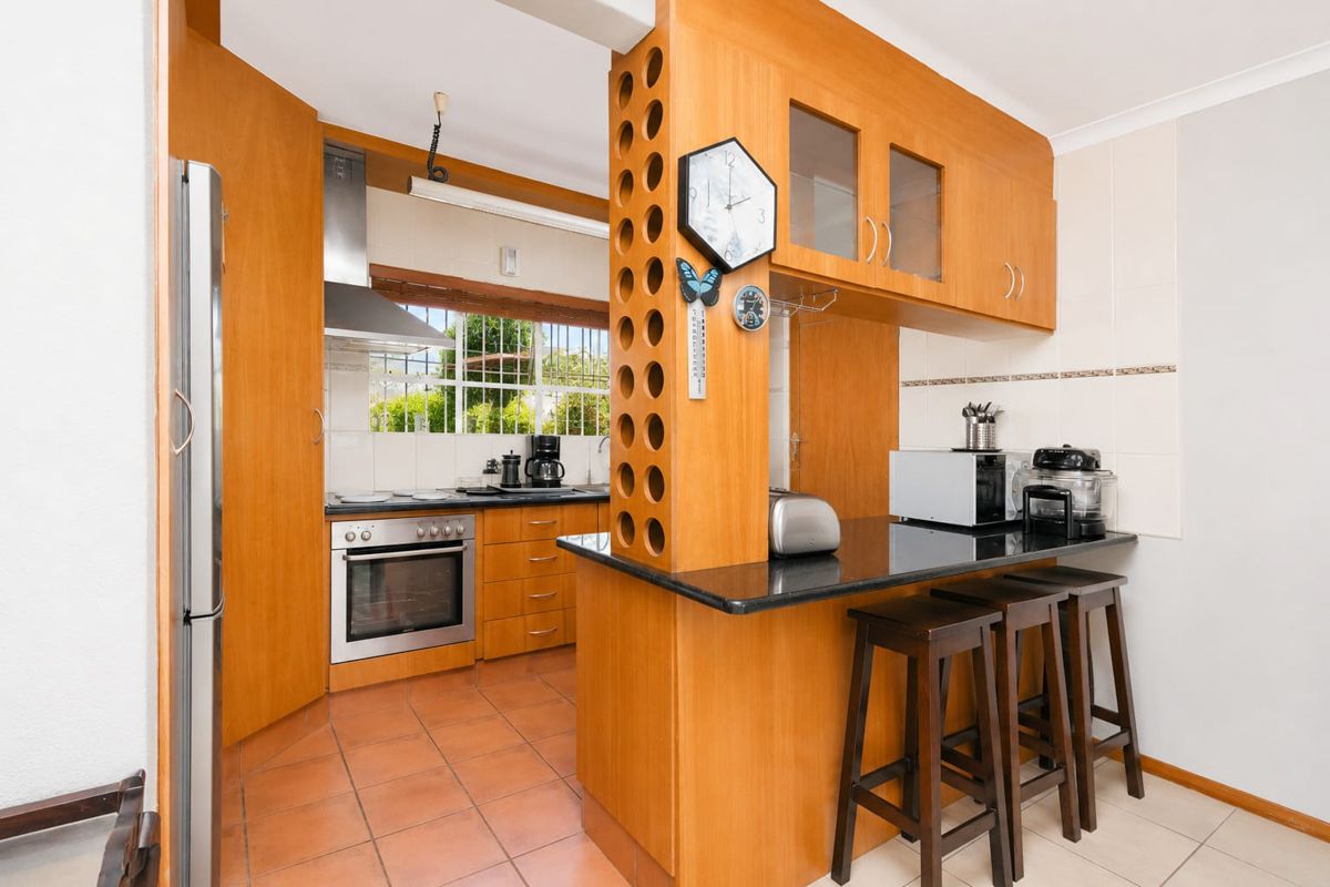 A functional kitchen featuring wood-finish cabinetry, granite countertops, a breakfast bar, and built-in stainless steel appliances with tiled flooring.
