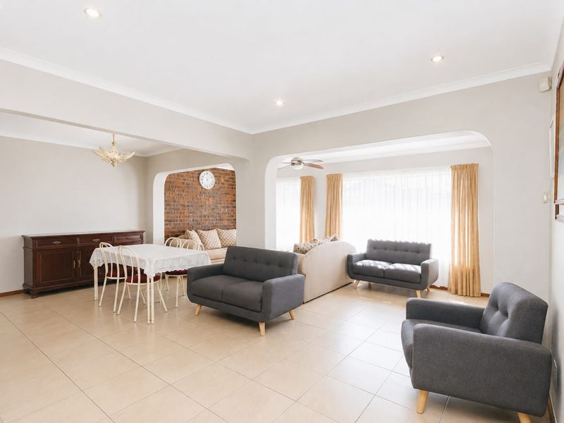 Spacious open-plan living and dining area featuring tiled floors, recessed lighting, and a characterful exposed brick feature wall.