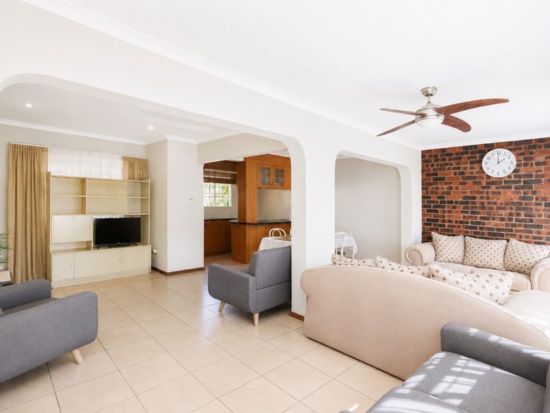 Spacious open-plan living area featuring tiled floors, an exposed brick feature wall, and arched transitions leading to the kitchen and dining space.