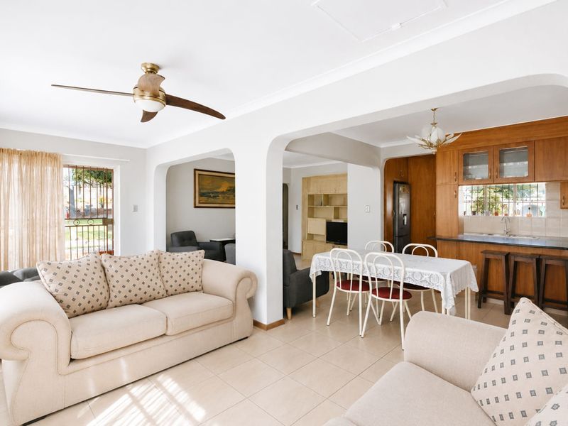 Open-plan living and dining area featuring tiled floors, a ceiling fan, and a functional kitchen with built-in cabinetry and a breakfast bar.