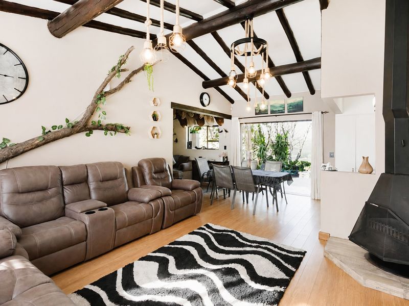 Open-plan living and dining area featuring exposed timber ceiling beams, a modern freestanding fireplace, and direct access to the outdoor patio through sliding glass doors.