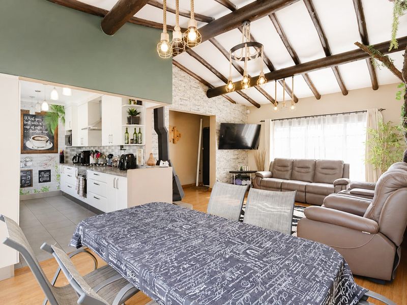 Spacious open-plan living and kitchen area featuring exposed timber ceiling beams, a stone feature wall, and modern cabinetry.