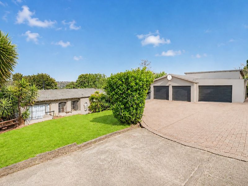 Front exterior view featuring a spacious paved driveway leading to a triple garage with roller doors and a well-maintained lawn area.