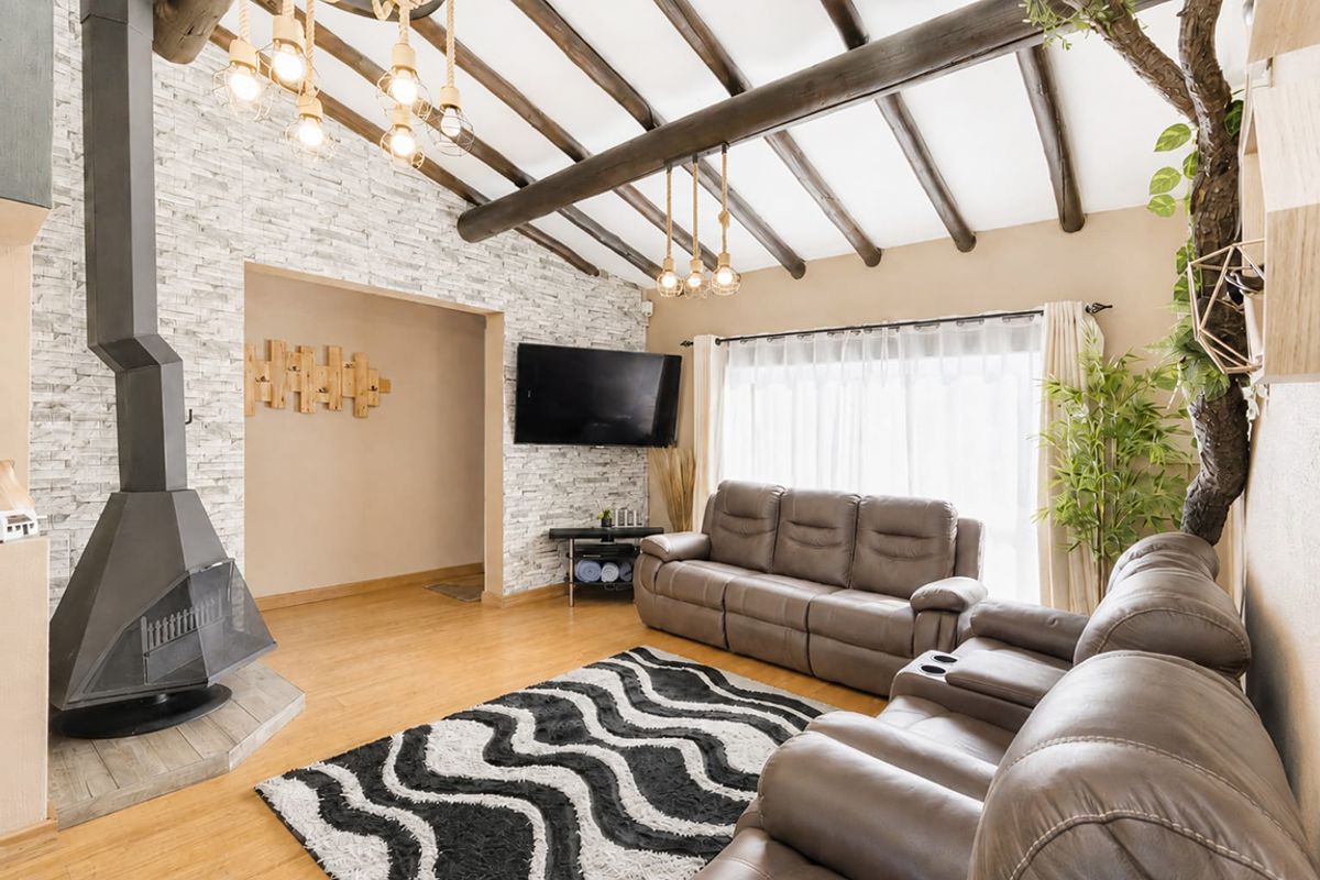 Cozy living room featuring exposed timber ceiling beams, a striking stone veneer feature wall, and a modern freestanding metal fireplace.