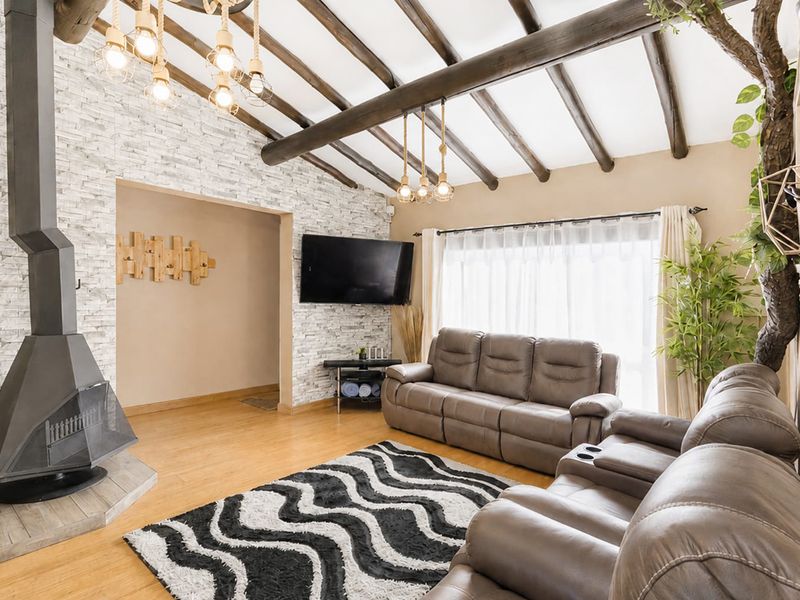 Cozy living room featuring exposed timber ceiling beams, a striking stone veneer feature wall, and a modern freestanding metal fireplace.