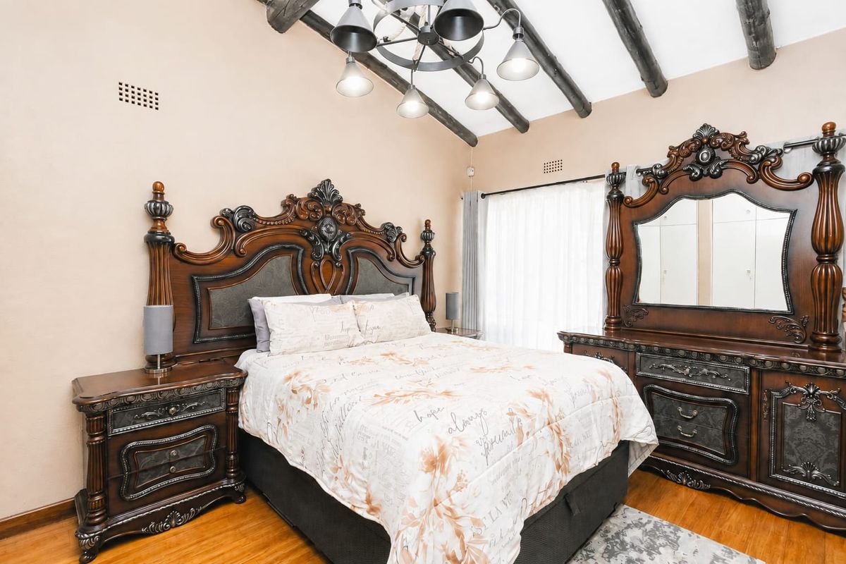 A well-maintained bedroom featuring exposed timber ceiling beams, laminate flooring, and a vaulted ceiling design.