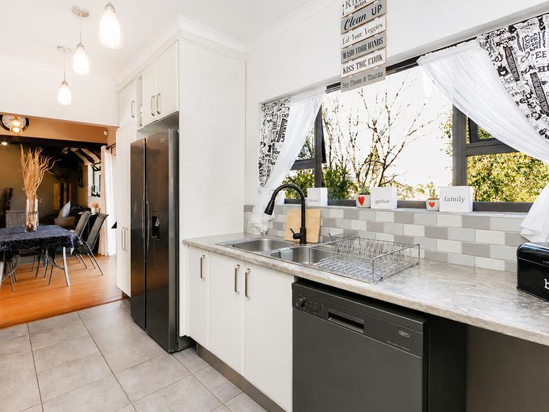 A functional kitchen featuring white cabinetry, stone-look countertops, a double sink with a modern black tap, and a stylish subway tile backsplash.