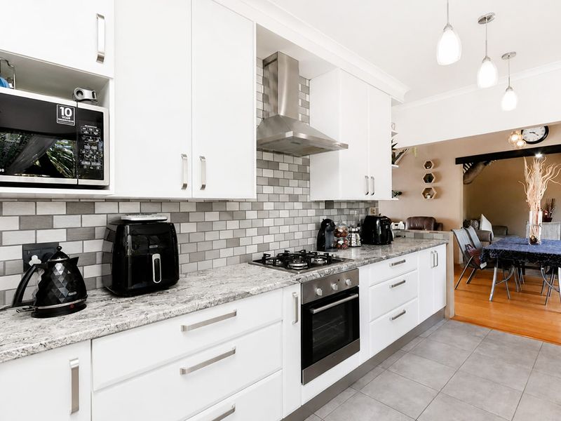 Modern kitchen featuring white cabinetry, granite countertops, subway tile backsplash, and stainless steel appliances, seamlessly flowing into the adjacent dining area.