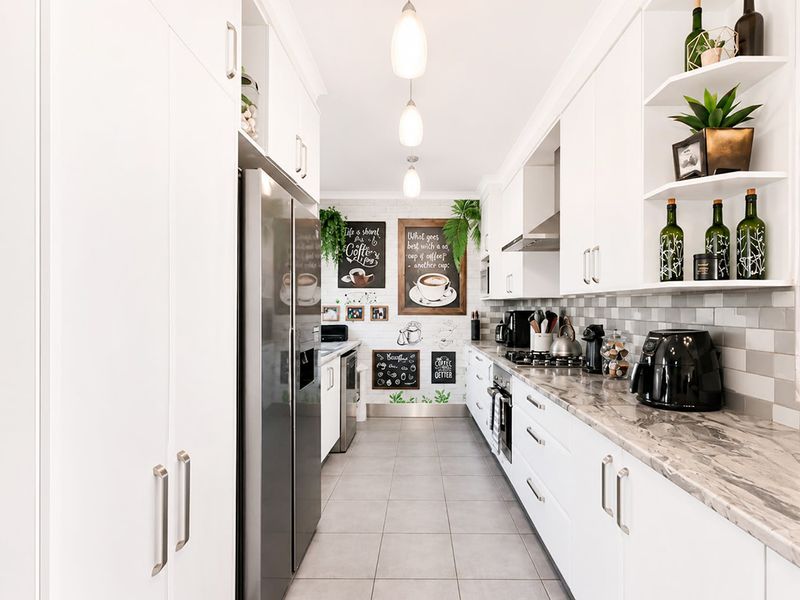 Modern galley-style kitchen featuring white cabinetry, stone-look countertops, gas cooktop, built-in oven, and stylish tiled backsplash with contemporary pendant lighting.
