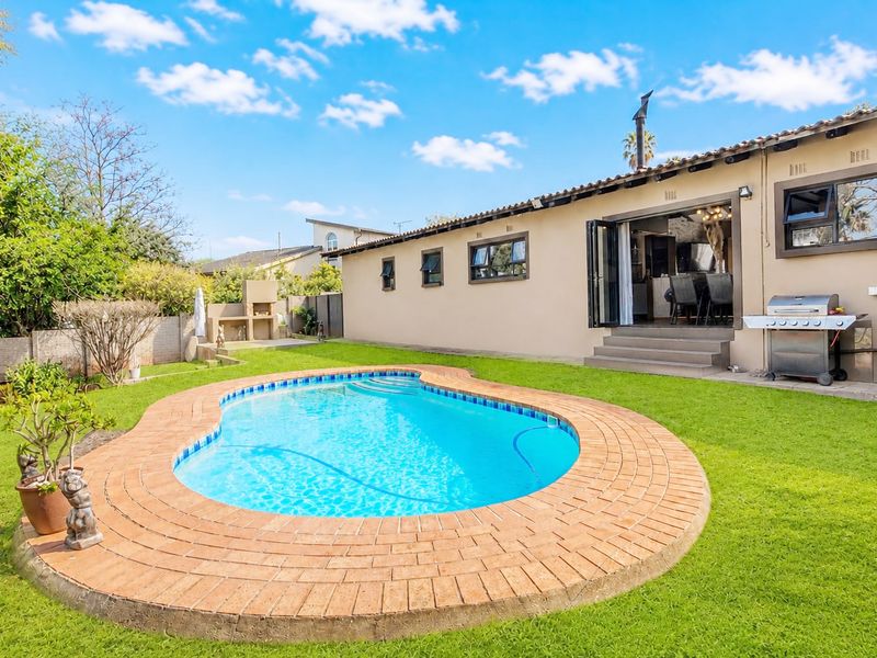 Rear garden featuring a swimming pool with brick coping, a built-in braai, and direct access to the home via bi-fold doors.