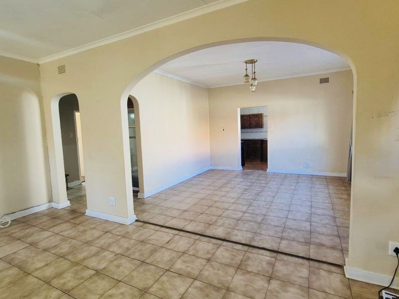 An empty open-plan living area featuring tiled flooring, arched architectural transitions, and neutral wall tones, offering a blank canvas for renovation.