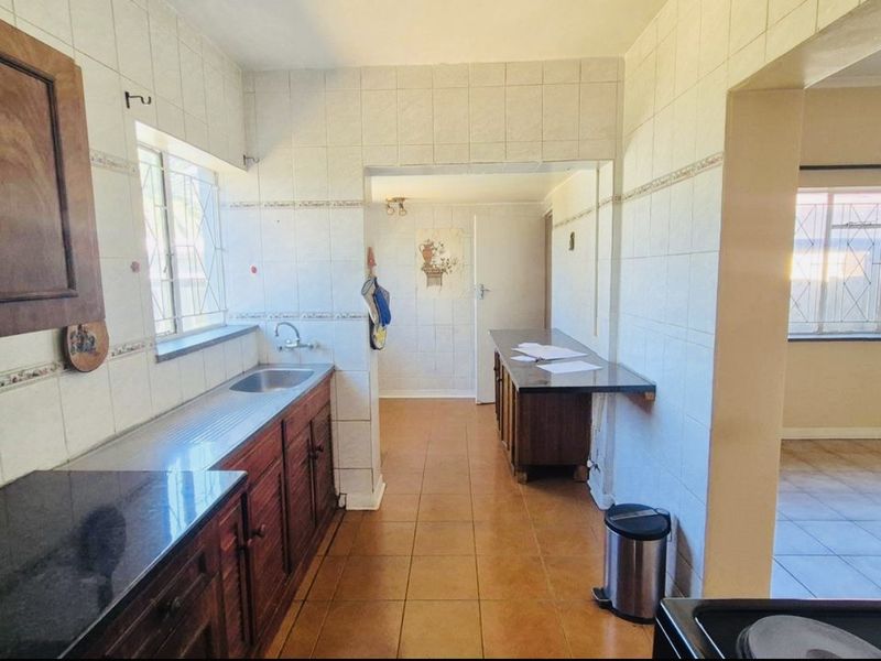 A dated kitchen featuring built-in wooden cabinetry, tiled walls, and tiled flooring, offering a functional layout with potential for modern renovation.