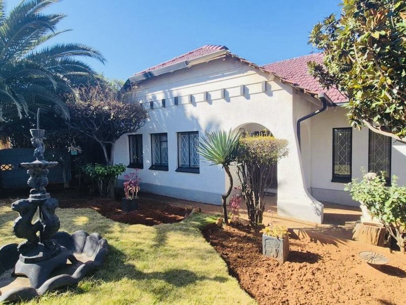 Front elevation of a charming house featuring a tiled roof, arched entrance, and classic leaded glass windows set within a landscaped garden.