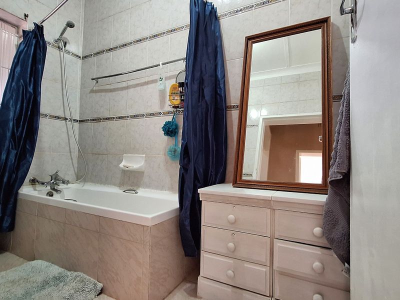 A functional bathroom featuring a built-in bathtub with shower mixer, tiled walls, and a window with a security gate.