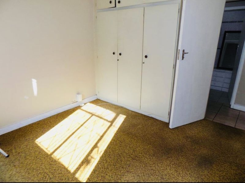 A vacant bedroom featuring built-in cupboards and carpeted flooring, awaiting updates to modernize the space.