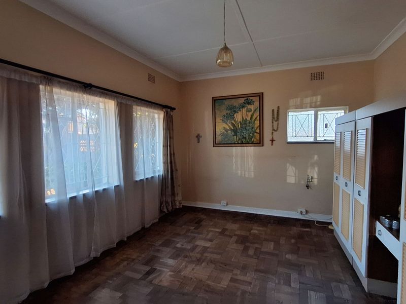 A bedroom featuring classic parquet flooring, built-in cupboards, and large windows with security bars, offering a functional and well-lit living space.