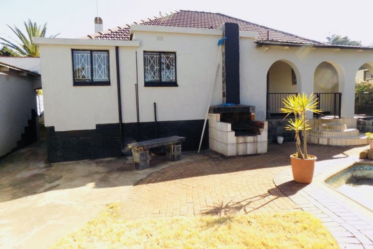 Rear exterior view of the house featuring a paved patio area, built-in braai, and arched veranda access.