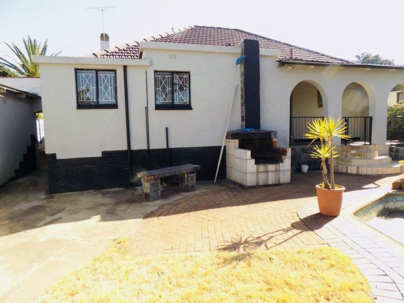 Rear exterior view of the house featuring a paved patio area, built-in braai, and arched veranda access.