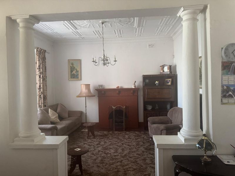 A traditional living room featuring a decorative ceiling, fireplace, and structural columns, offering a classic layout with potential for modernization.